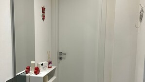 A hallway with a white door, a mirror, a white shelf with decorative items, and a white wall. - Vacation House at Mely's (Marsala)