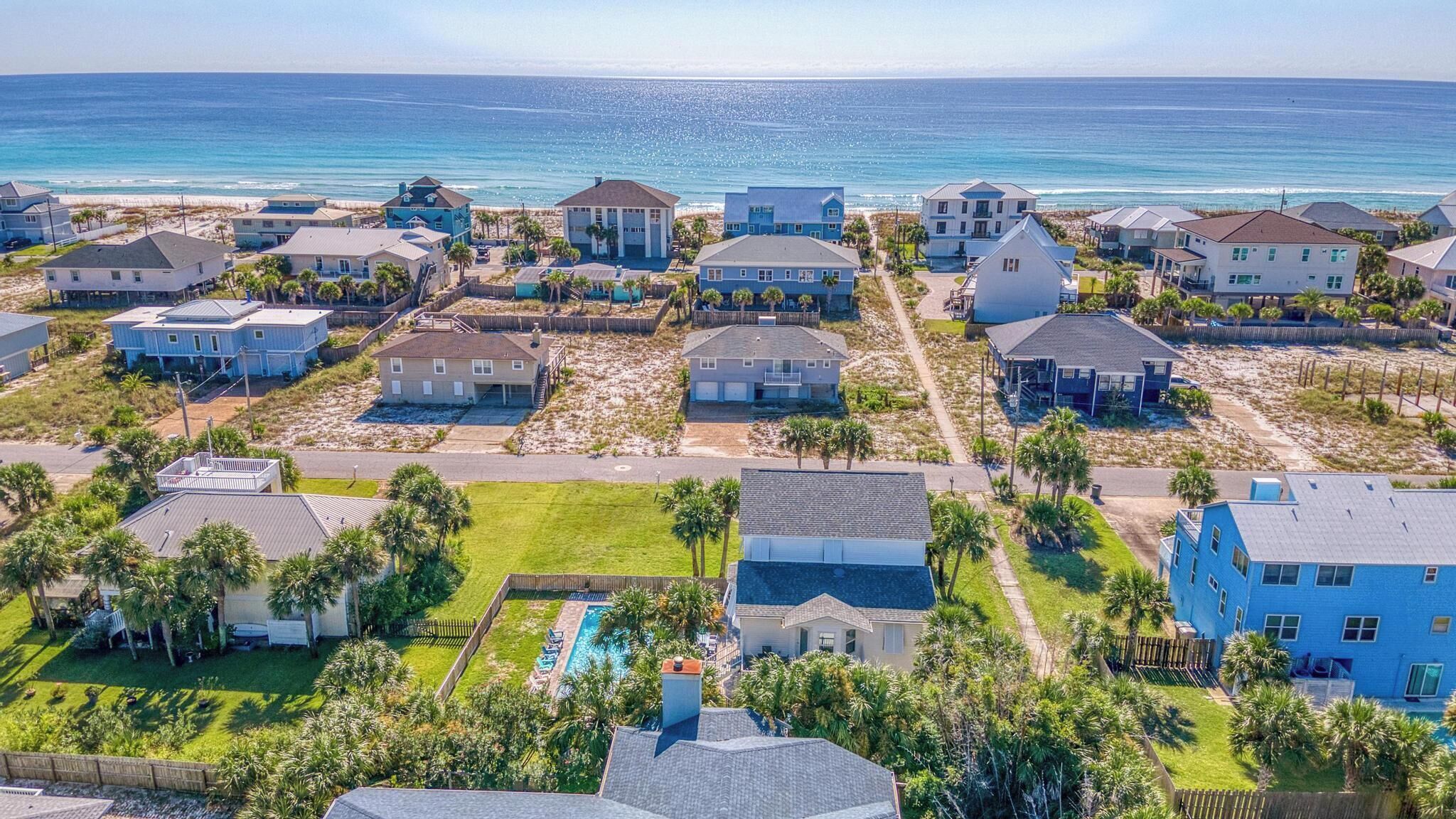 A coastal residential area with houses, a swimming pool, and a beach in the background.