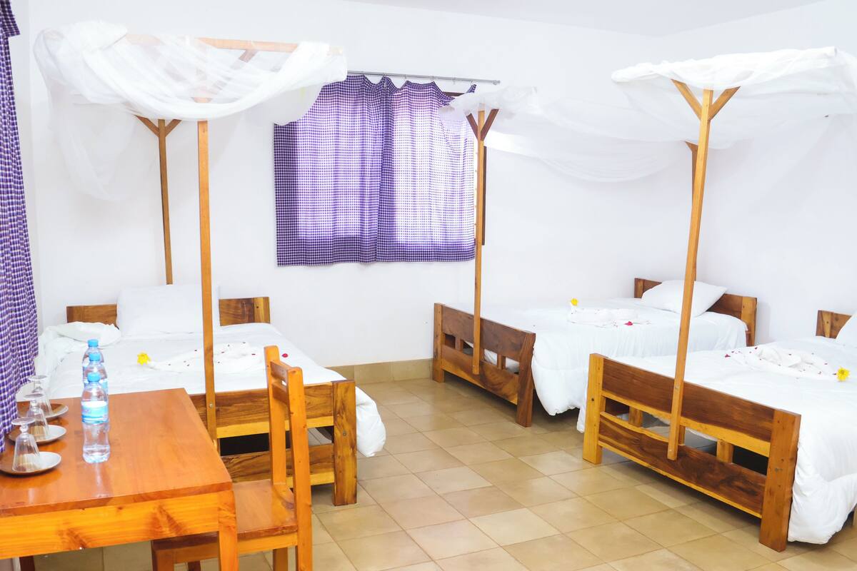 A room with two wooden beds, a wooden table with chairs, and a small table with a water bottle and glasses.