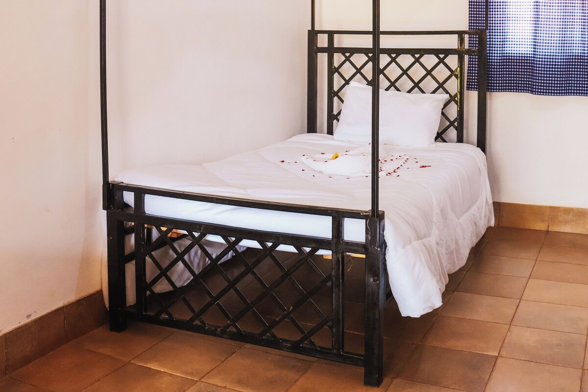 A four-poster bed with a canopy, white bedding, and a checkered curtain in the background.