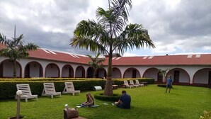 A courtyard with a palm tree, lounge chairs, and a building with arched windows. - Stc.Safari lodge (Karatu)