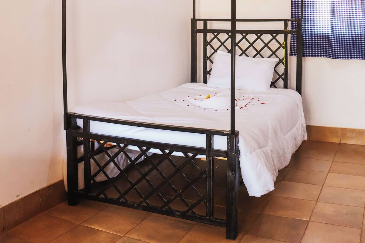 A four-poster bed with a canopy, white bedding, and a checkered curtain in the background.