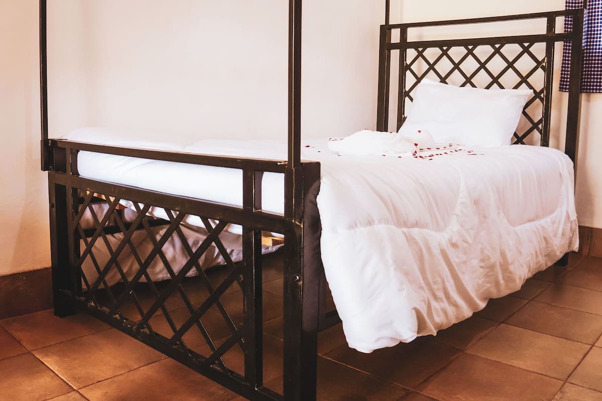 A single bed with a black metal frame and white bedding, including a pillow and a blanket.