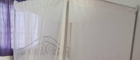 A single bed with a mosquito net in a room with white walls and a tiled floor.