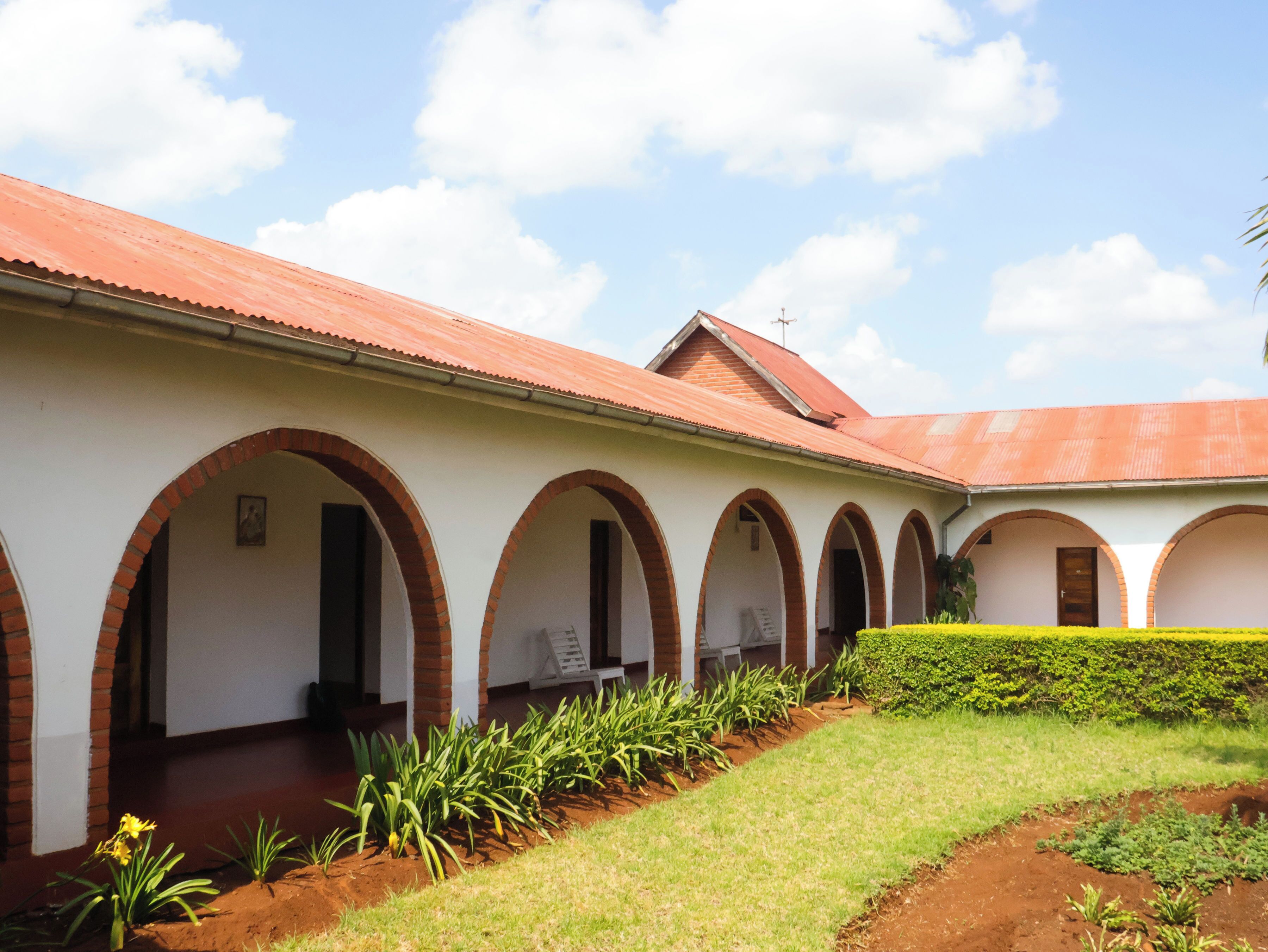 A building with a series of arched doorways, a red roof, and a garden area with plants and a pathway.