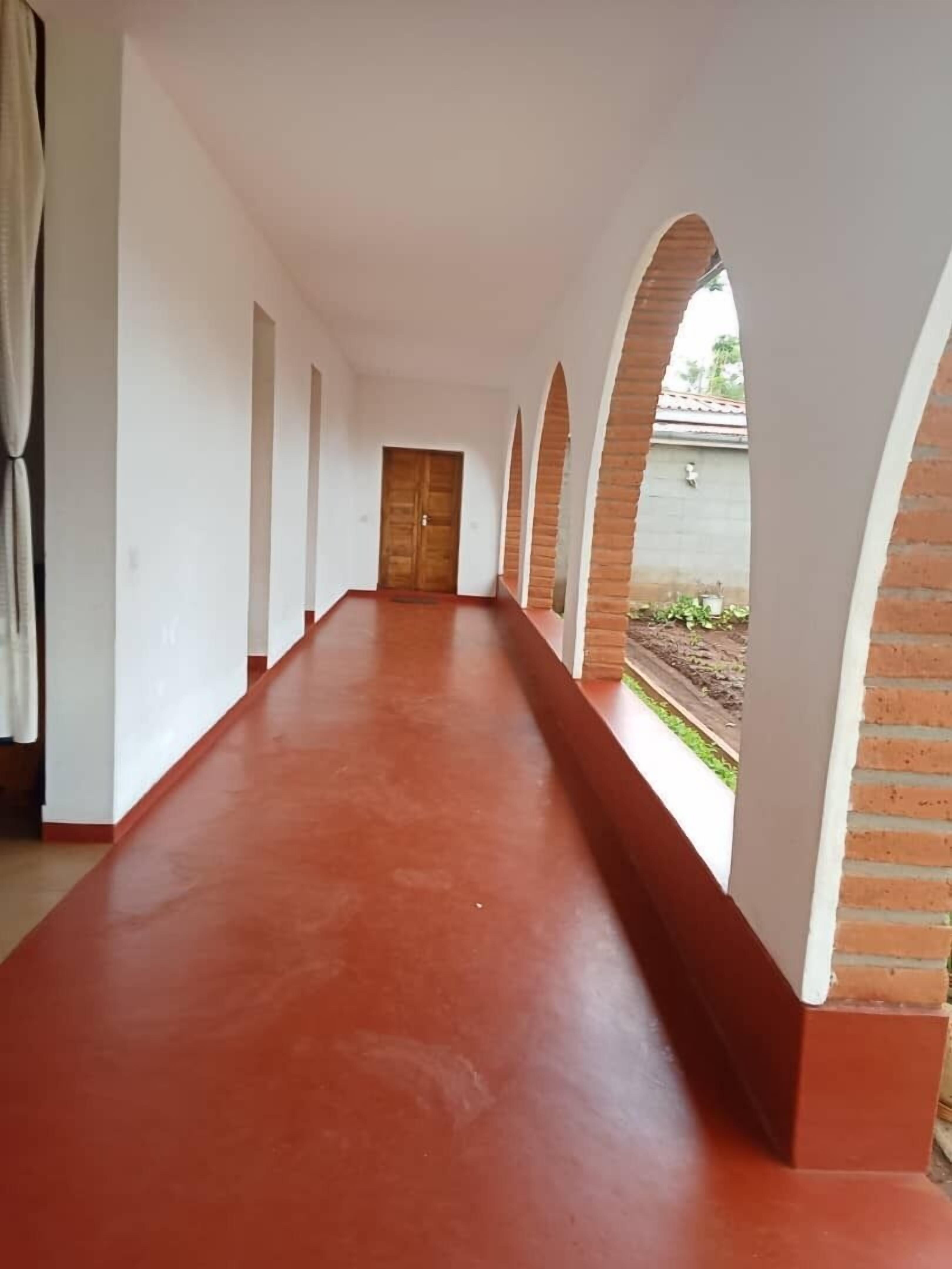 A corridor with a red floor, white walls, and brick arches.