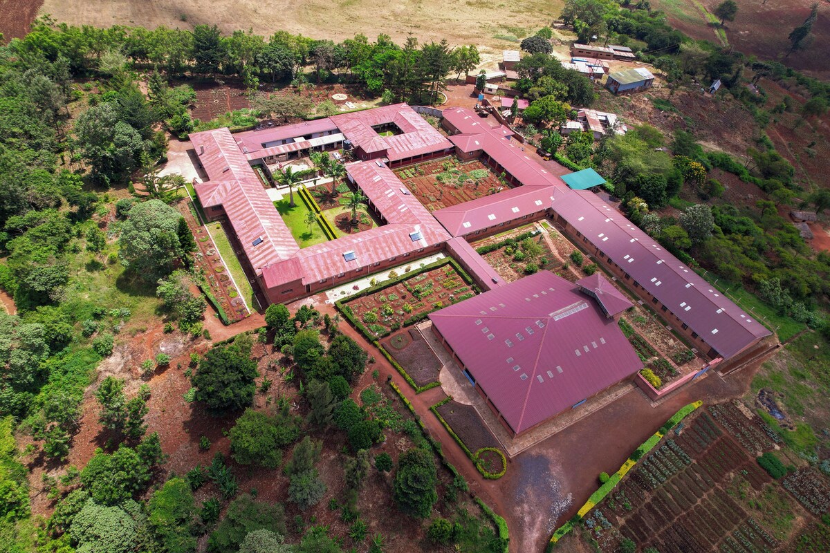 An aerial view of a large, rectangular building with multiple sections, surrounded by dense greenery and trees.