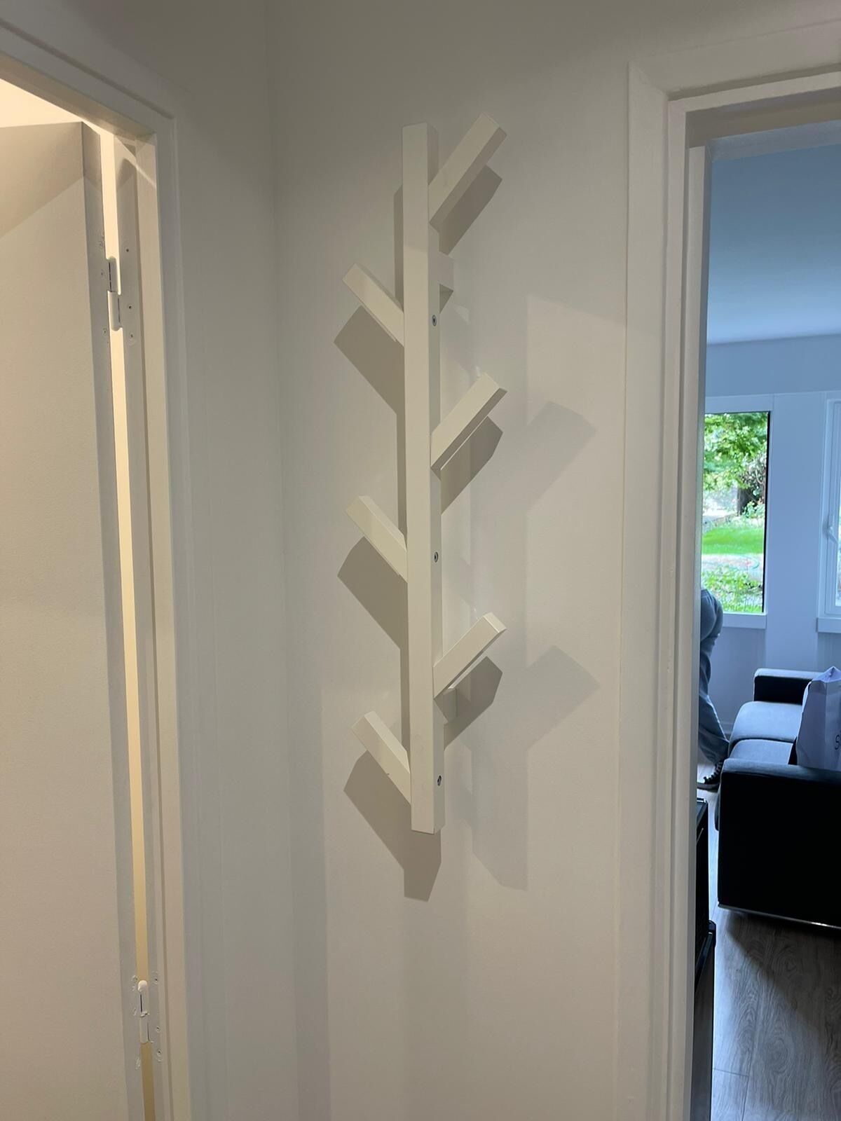 Un couloir avec une étagère murale blanche et une porte donnant sur une pièce d’où l’on peut admirer la verdure à l’extérieur.