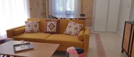 A living room with a yellow sofa, patterned cushions, a coffee table, and a small stool.