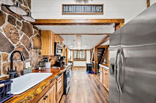 A kitchen with a stone wall, wooden cabinets, a stainless steel refrigerator, and a 'DO NOT FEED THE BEARS' sign. - See Bears Daily | Family Cabin + Game Room (Gatlinburg)