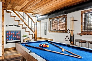 Une table de billard avec des billes et des queues, un escalier, et une table de billard fixée au mur, avec un porte-billes.