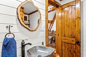 Une salle de bain rustique avec un lavabo en pierre, une porte en bois et un miroir avec un cadre en bois.
