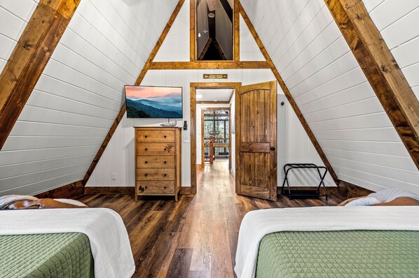 Une pièce avec des poutres en bois, un lit, une commode, un téléviseur et une porte donnant sur un couloir.