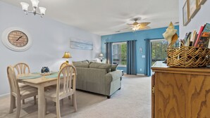 A living room with a dining table, chairs, a sofa, a chandelier, and a ceiling fan. - Short Stays in Summer - Pool - Seven Oaks 9-302 (North Myrtle Beach)