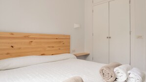 Et soveværelse med sengegavl i træ, seng med hvide sengetæpper, et natbord og en garderobe.