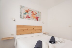 Une chambre d’hôtel avec une tête de lit en bois, une couvre-lit blanche et une peinture abstraite aux couleurs vives accrochée au mur.