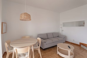 Una sala de estar moderna con una mesa de comedor redonda, dos sillas, un sofá gris, una pequeña mesa redonda de centro y una lámpara colgante de fibras.