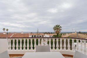 Une terrasse dotée d’une balustrade blanche, de chaises blanches et offrant une vue sur les bâtiments côtiers et les palmiers.