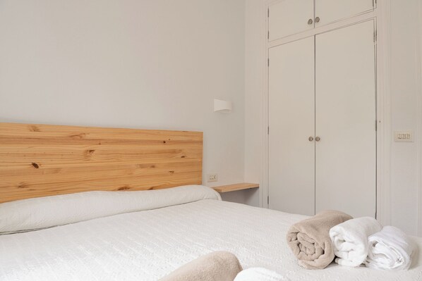 Une chambre à coucher avec une tête de lit en bois, un lit avec une literie blanche, une table de chevet et une armoire.
