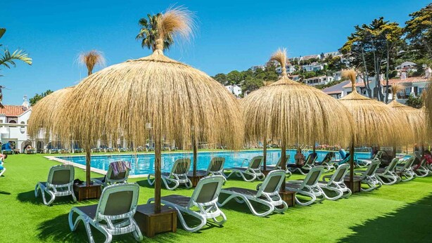 Zona junto a la piscina con sillones de descanso y sombrillas de paja.