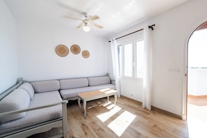 A modern living room with a gray sofa, a wooden coffee table, a ceiling fan, and three wall-mounted woven decorations.