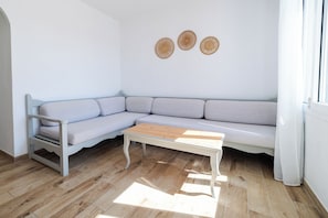 A modern living room with a light grey sectional sofa, a wooden coffee table, and a small white table. There are three woven wall decorations and a window with white curtains.