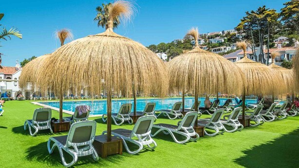 A poolside area with lounge chairs and thatched umbrellas, a swimming pool, and a green lawn. - Son Bou Gardens Plus (Son Bou)