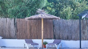 A pool area with two lounge chairs, a thatched umbrella, and a bamboo fence.
