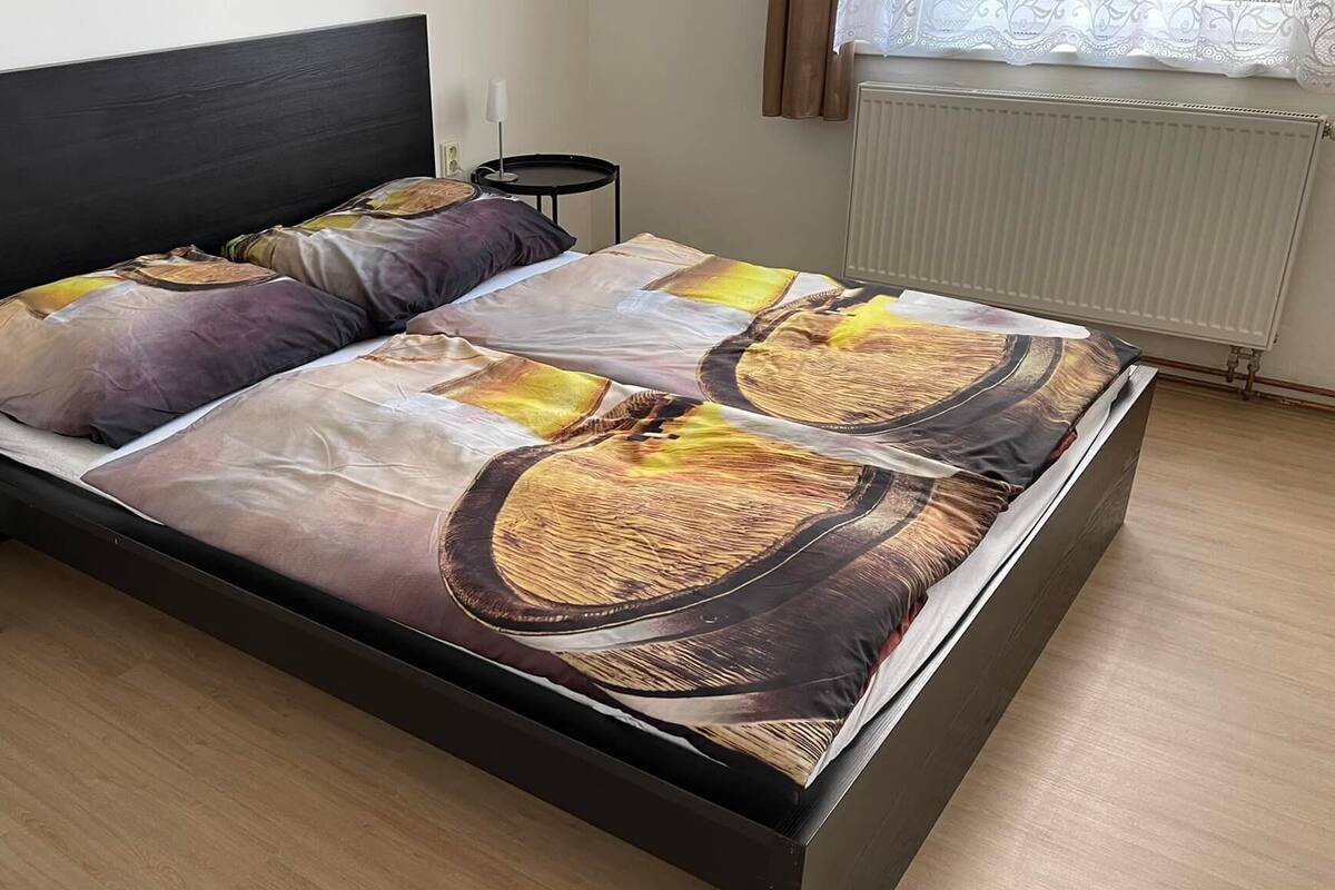 Una cama con cabecera negra y colcha estampada. Hay dos mesitas de noche, una a cada lado de la cama.