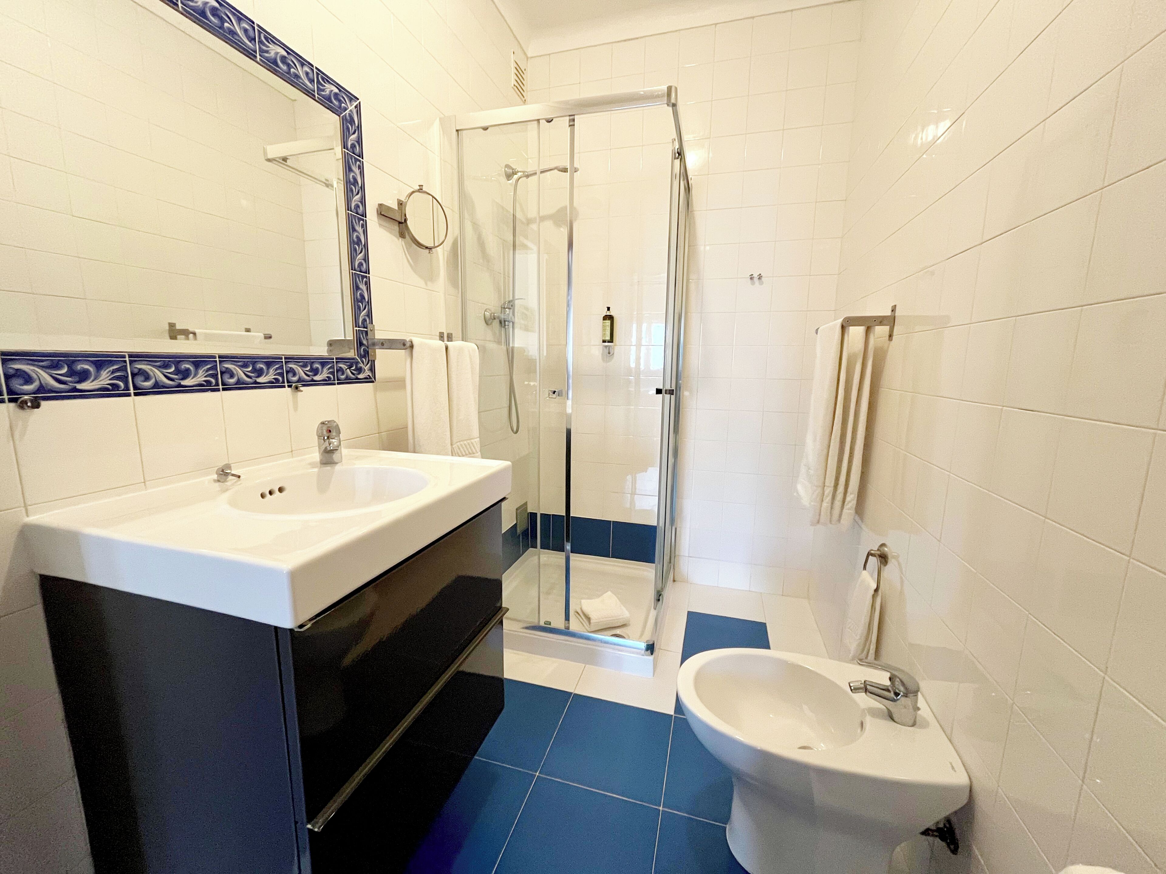 A bathroom with a double sink, a glass shower enclosure, and a bidet.
