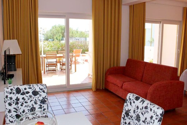 A room with a red sofa, two patterned armchairs, a table, and a lamp.