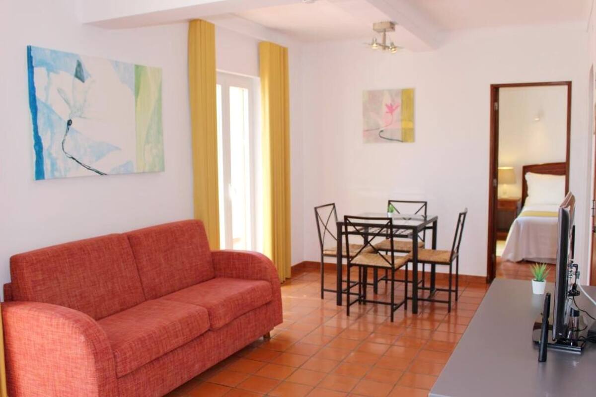 A room with a red sofa, a dining table with chairs, a TV, and artwork on the walls.