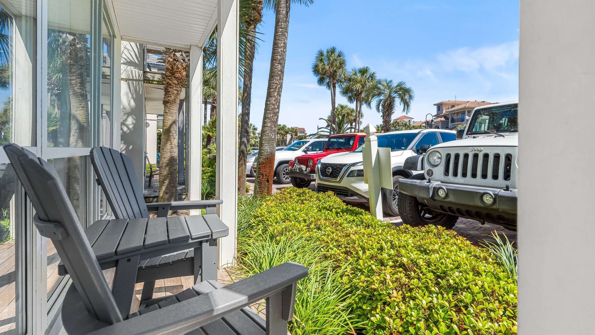 A covered outdoor seating area with a chair, a building with large windows, and parked vehicles including a white SUV and a red Jeep.