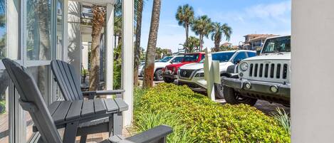 A covered outdoor seating area with a chair, a building with large windows, and parked vehicles including a white SUV and a red Jeep.
