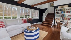 Una sala de estar con un sofá blanco, un reposapiés azul a rayas, una estantería y una escalera.