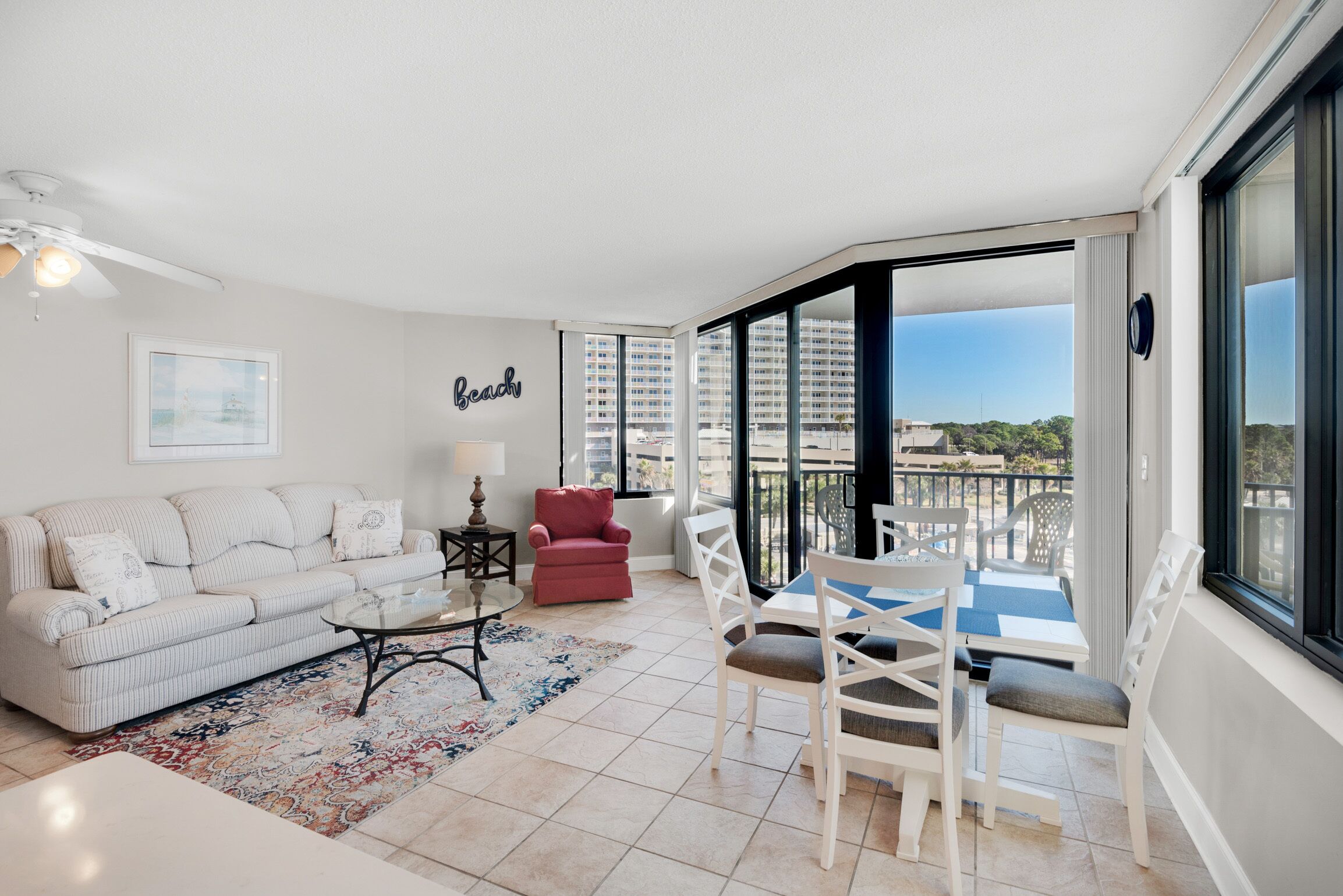 Un salon moderne avec un canapé, un fauteuil rouge, une table basse et un balcon offrant une vue sur la ville.