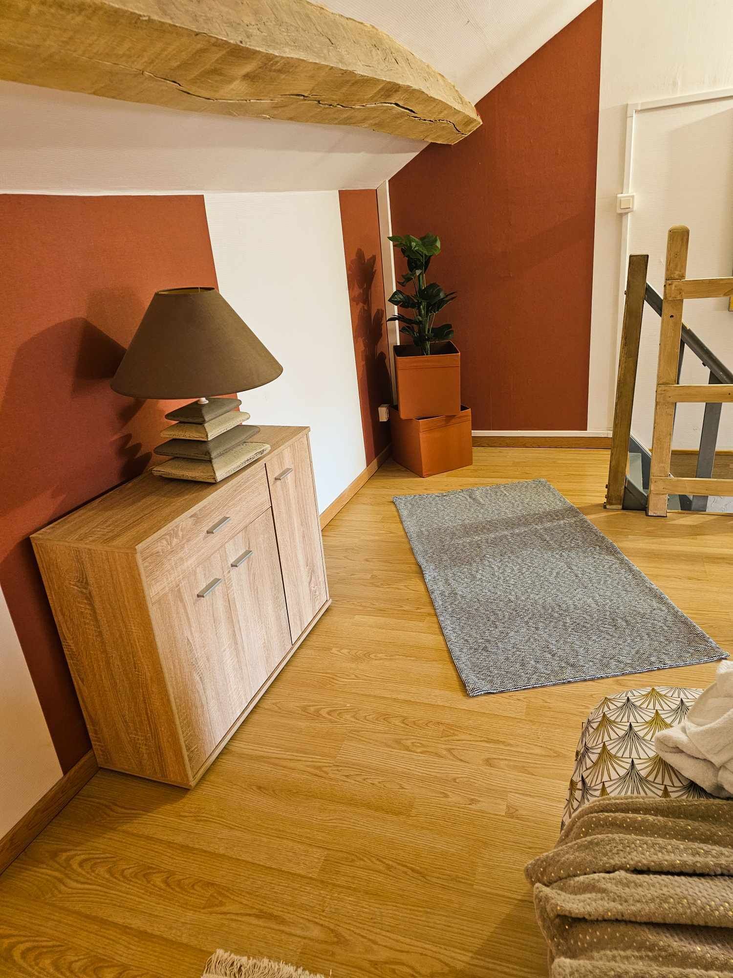 Ein Zimmer mit einem Holzschrank, einer Lampe, einer Pflanze, einem gemusterten Teppich und einer Treppe.