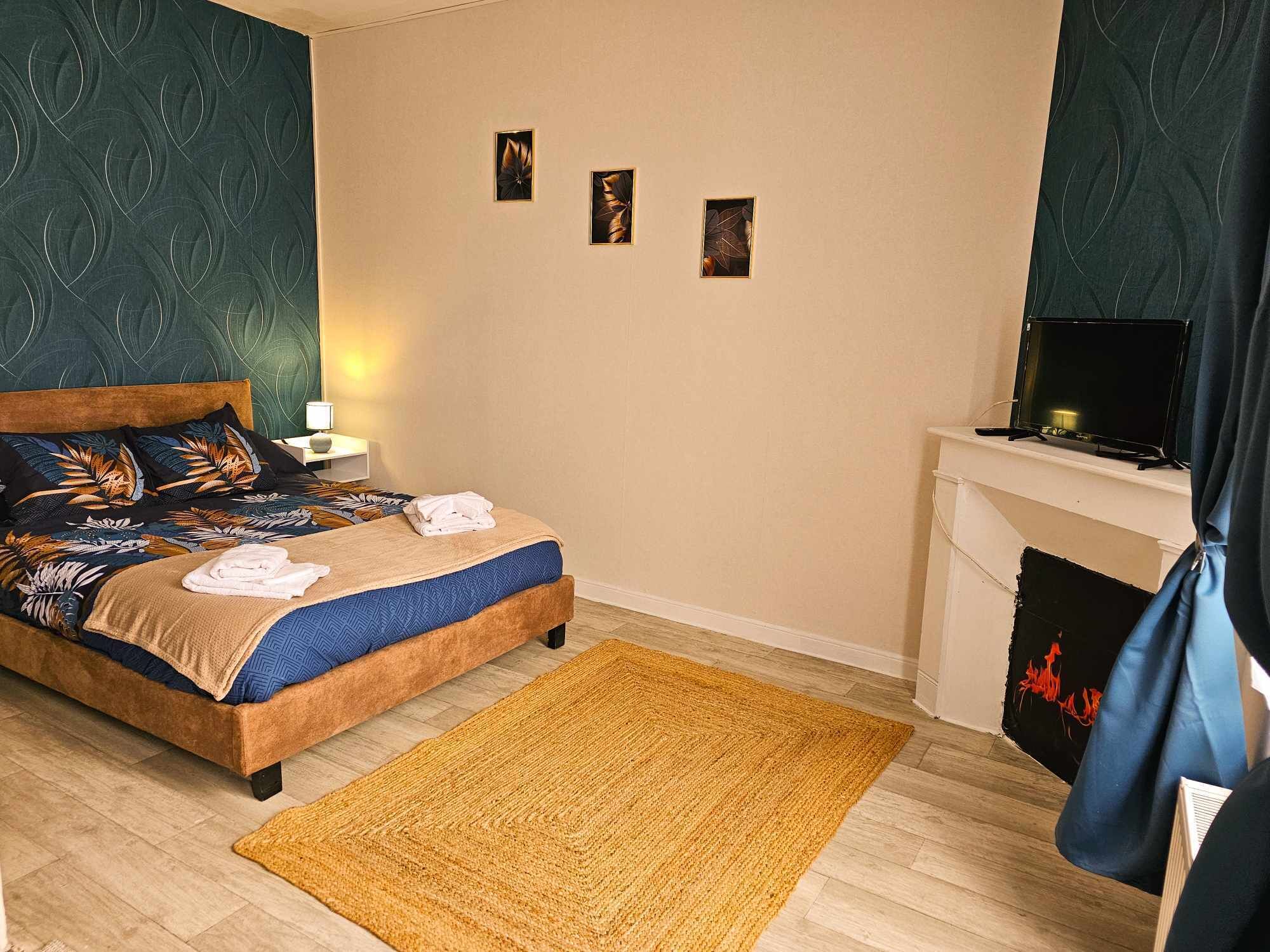 A bedroom with a bed, a nightstand, a TV, and a fireplace.