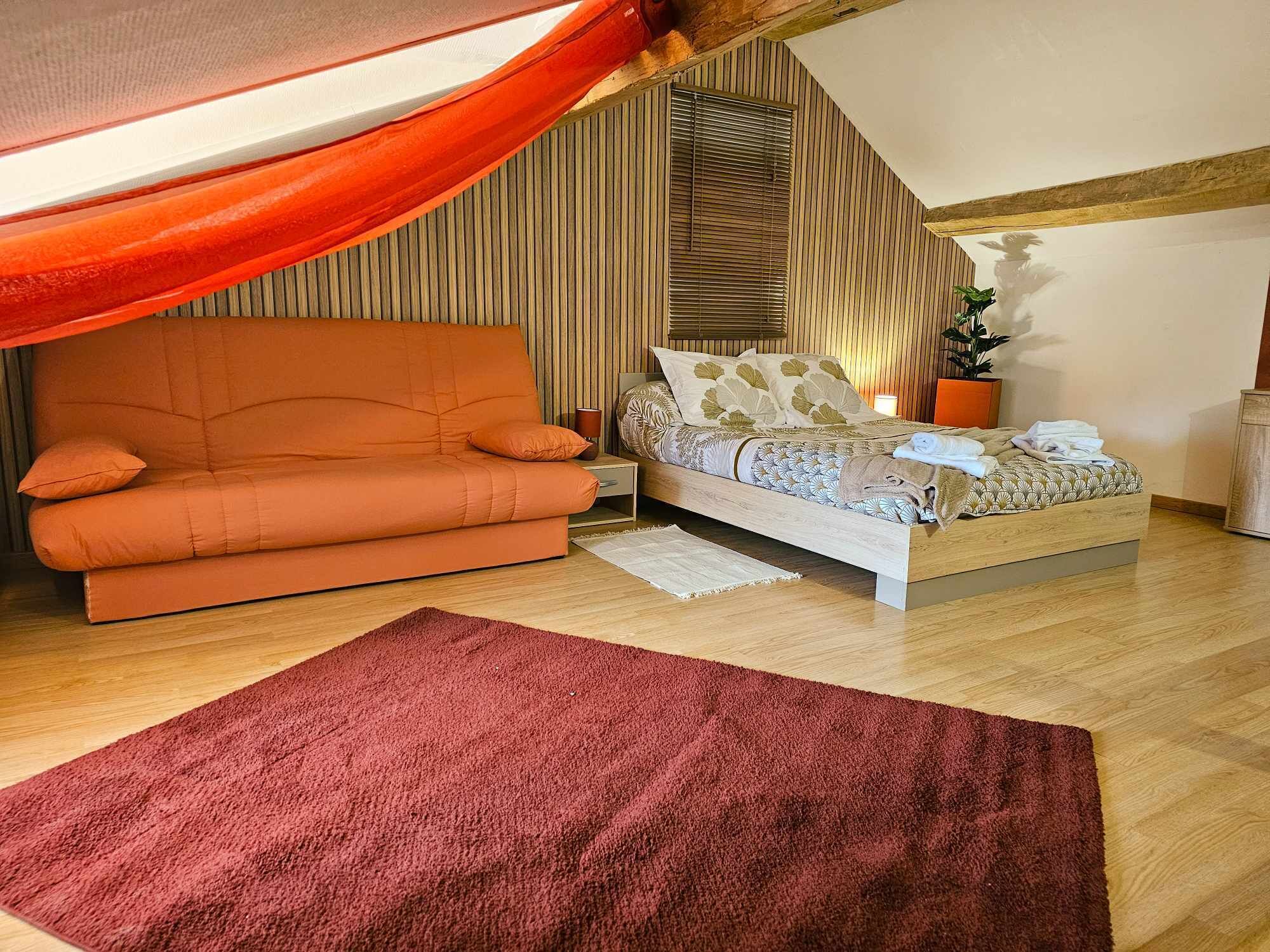 Ein Schlafzimmer mit einer Couch, einem Bett, Holzboden, einem roten Teppich und einem Fenster mit Jalousien.