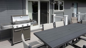 Een terras buiten, met een barbecue, een tafel en stoelen.