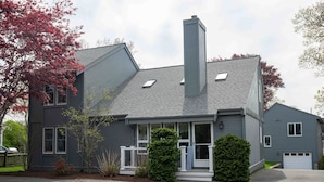 Een huis met twee verdiepingen, een grijze gevel, een schoorsteen en een voortuin.
