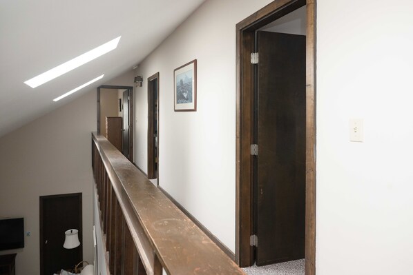 A hallway with a wooden railing, a ceiling light, a framed picture, and a door.