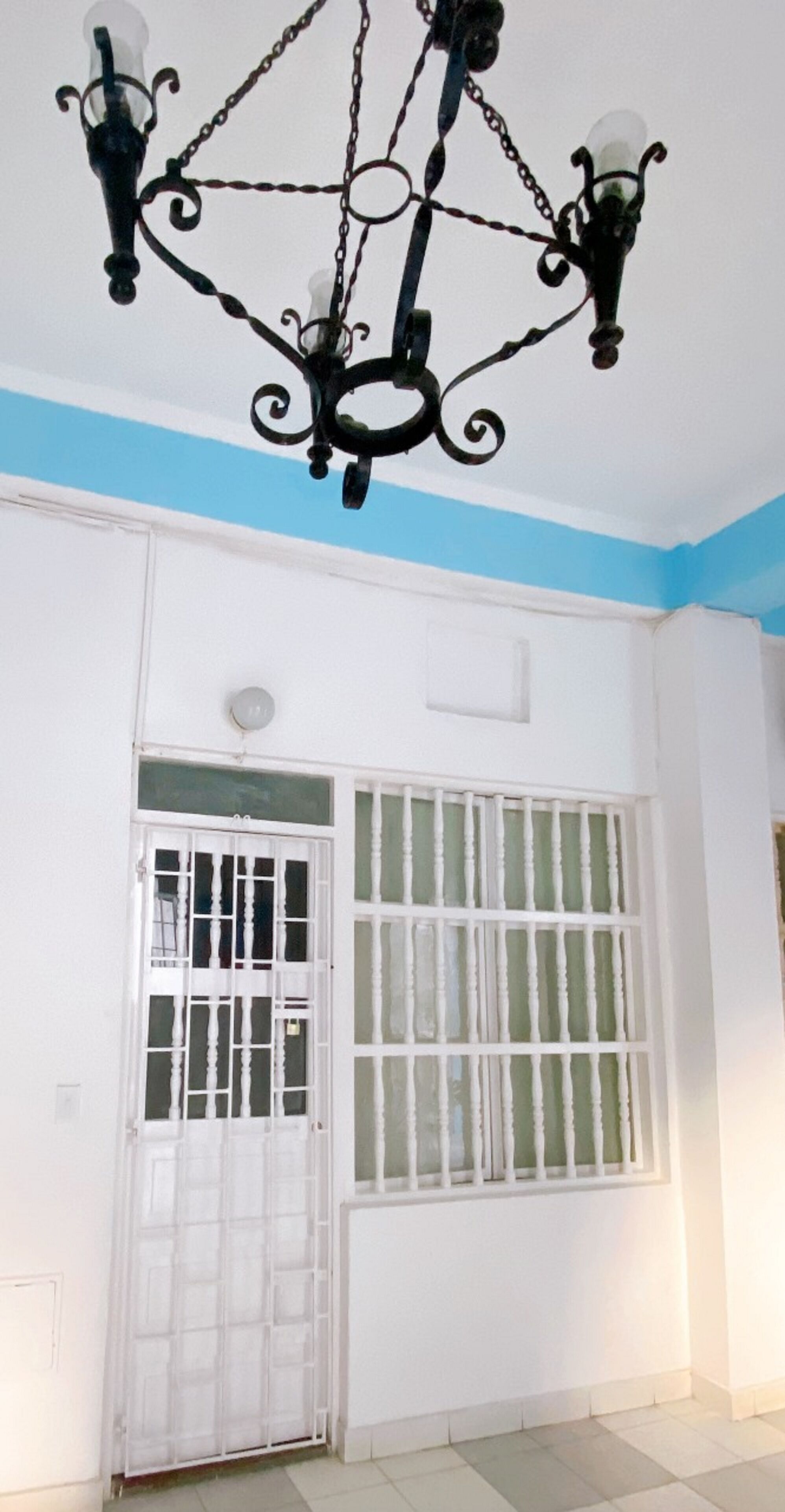 Una stanza con una porta bianca, una finestra con inferriate bianche e un lampadario nero.