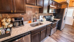 A modern kitchen with dark wooden cabinets, a granite countertop, stainless steel appliances, and a built-in oven.