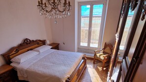 A bedroom with a large bed, a chandelier, a wooden chair, and a large mirror. - Apartment-Castro Pretorio 2 rooms (Roma)