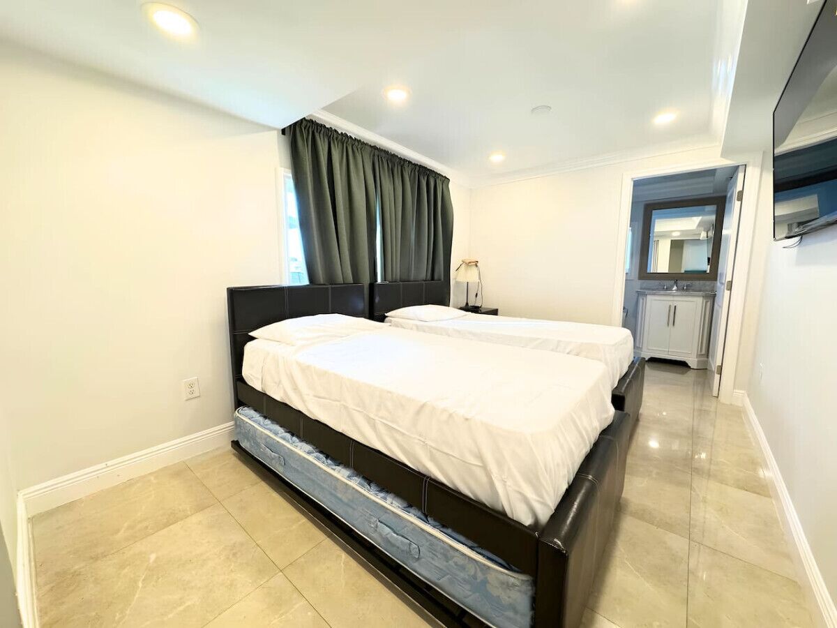 A modern bedroom with a large bed, a bedside table, and a small bathroom visible through an open door.