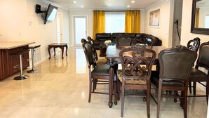 Un espace repas avec une table ronde et six chaises, un coin bar avec des tabourets et un téléviseur fixé au mur.