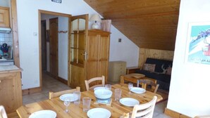 A dining area with wooden tables and chairs, a kitchen area with cabinets, and a loft bedroom with a bed and a view. - 3rd floor, parking, tv, ski locker, 38m², Les Contamines-Montjoie (Les Contamines-Montjoie)