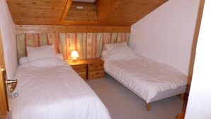A bedroom with two single beds, a wooden ceiling, a small bedside table with a lamp, and a window with curtains. - 3rd floor, parking, tv, ski locker, 38m², Les Contamines-Montjoie (Les Contamines-Montjoie)