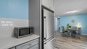 A kitchen with a microwave, refrigerator, and white cabinets.